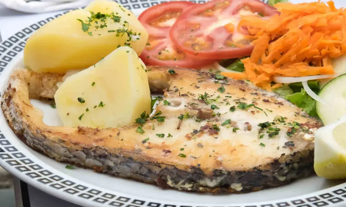 Un succulento pesce spada al forno, accompagnato da patate bollite, pomodori freschi, carote grattugiate e un'insalata leggera.