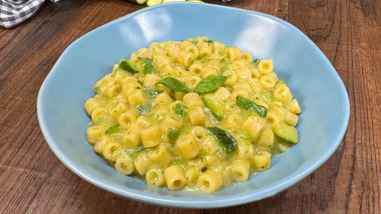 Un piatto di pasta con zucchine e basilico, cremoso e invitante, servito in una ciotola azzurra su un tavolo di legno.