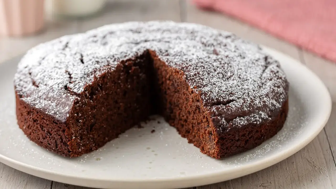 Una fetta è stata tolta da una torta al cioccolato morbida, cosparsa di zucchero a velo.