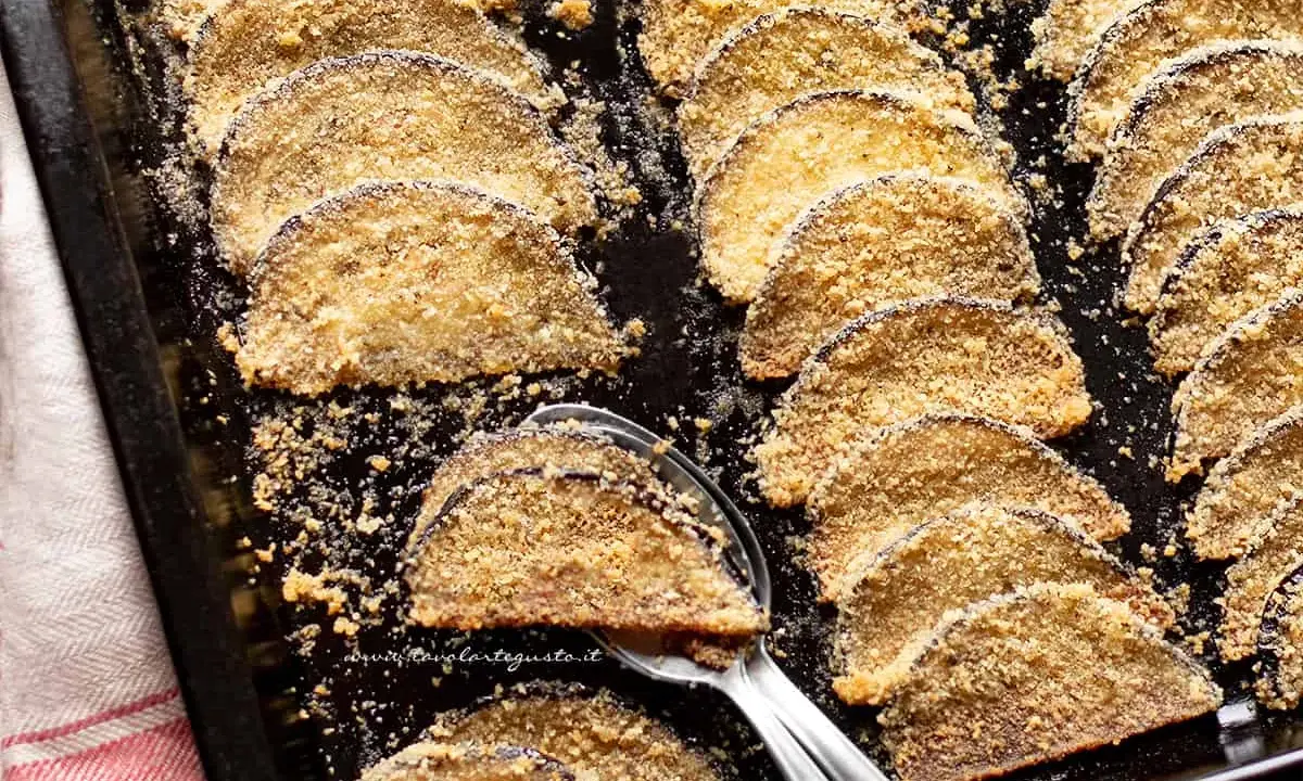 Fette di melanzane al forno, dorate e croccanti, disposte su una teglia. Un contorno saporito e leggero.