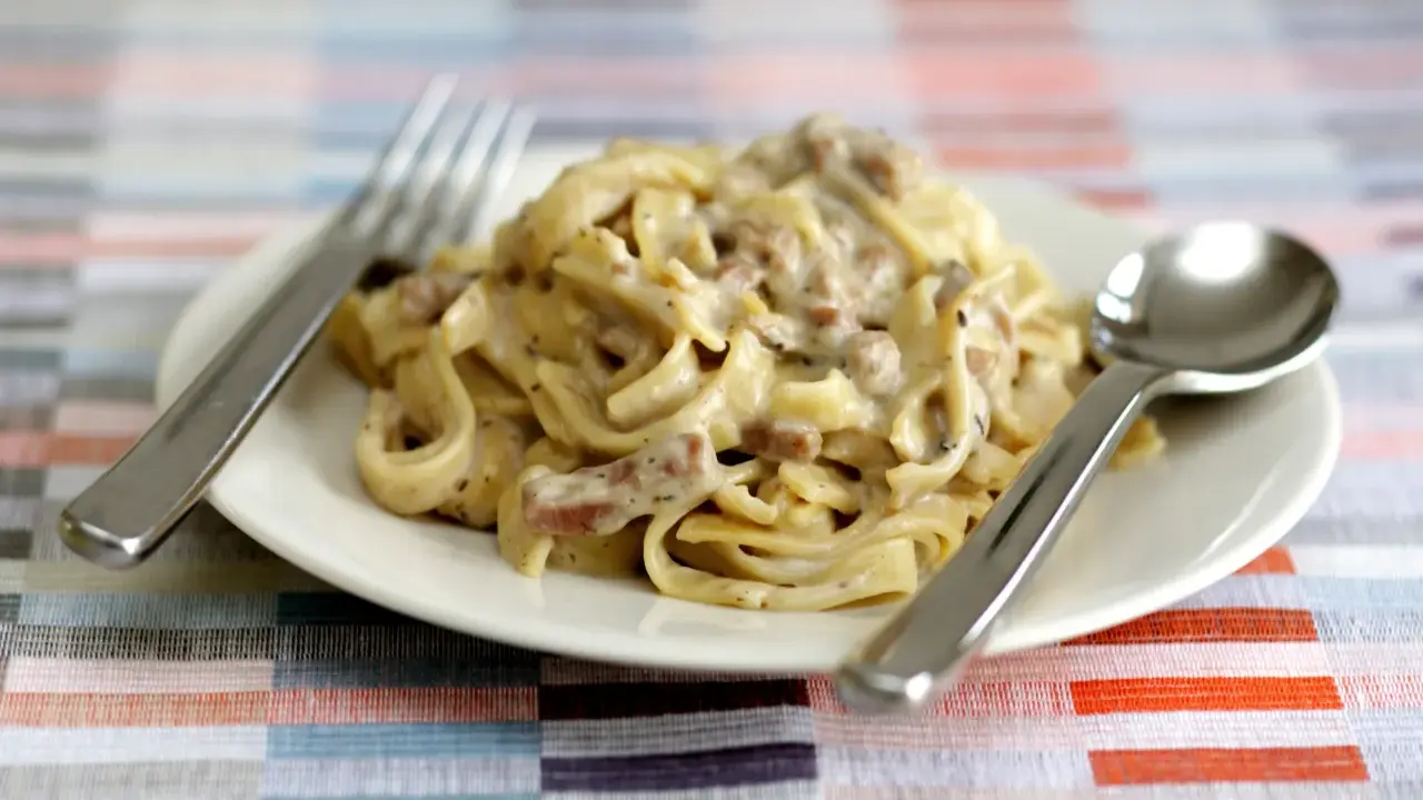 Un piatto di tagliatelle ai funghi cremose, con forchetta e cucchiaio pronti per gustare questo delizioso primo.