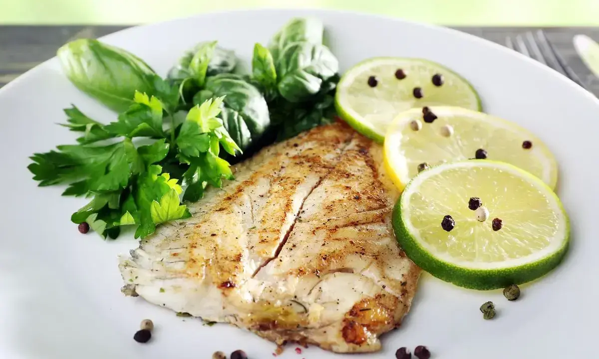 Un delizioso filetto di pesce san pietro grigliato, guarnito con erbe fresche, fette di limone e lime con pepe nero.