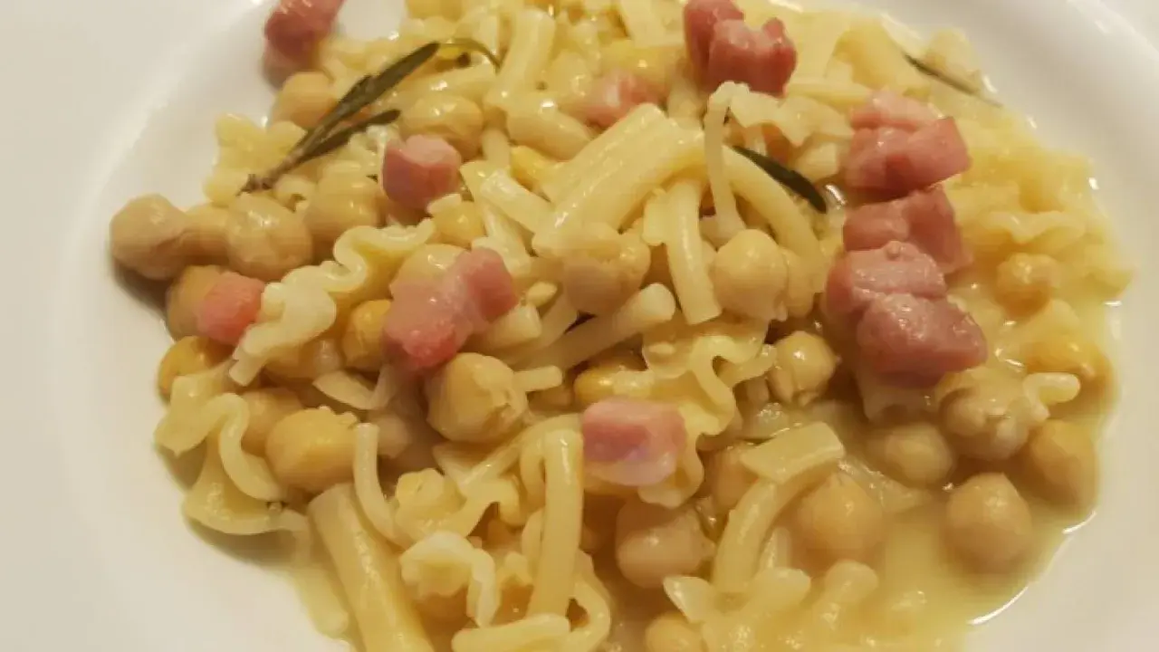 Piatto di pasta e ceci in scatola, con cubetti di pancetta e un rametto di rosmarino.