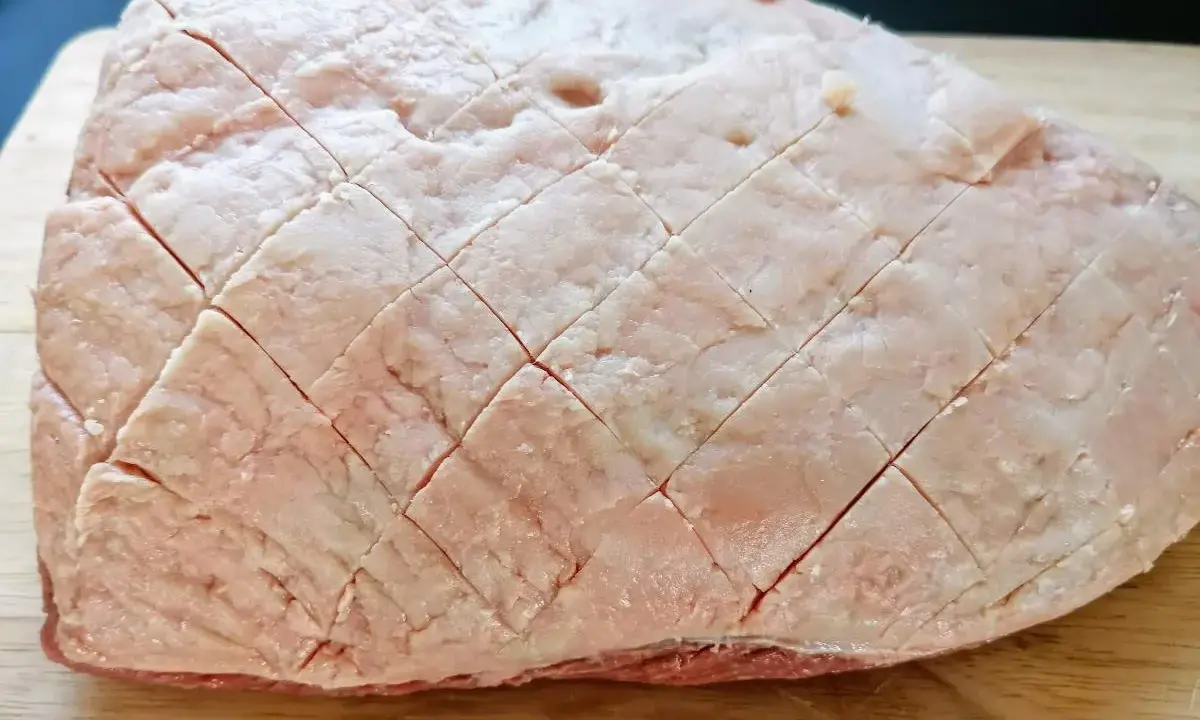 Un pezzo di picanha alla griglia, con la sua copertura di grasso incisa a rombi, pronto per essere cotto su un tagliere di legno.