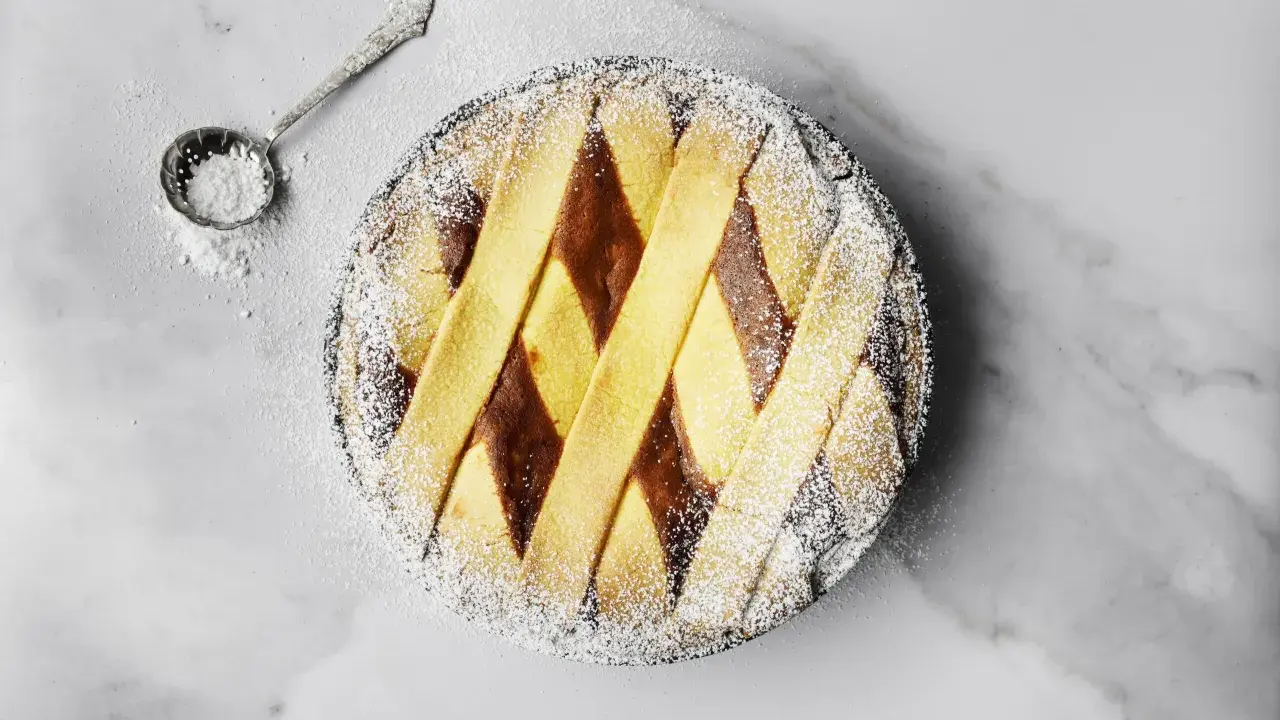 Pastiera napoletana pronta, cosparsa di zucchero a velo. Un cucchiaino d'argento è pronto per decorare, mostrando come si fa la pastiera.