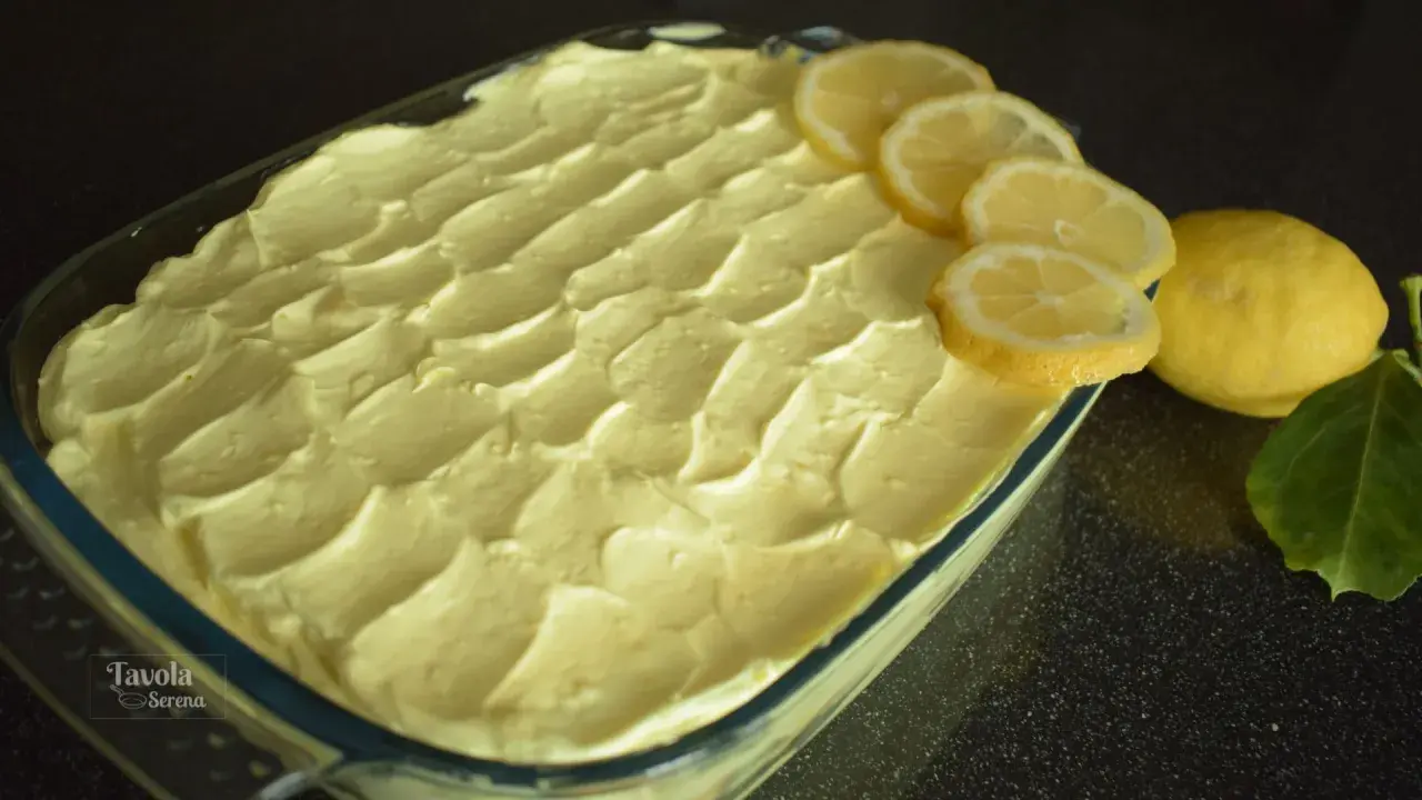 Un invitante tiramisù al limone, guarnito con fette di limone fresco e limoni interi, pronto per essere gustato.