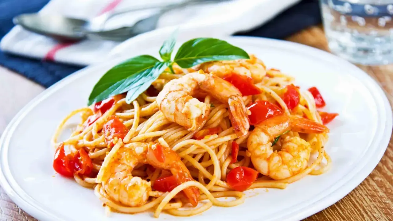 Spaghetti con gamberetti succulenti, pomodorini freschi e basilico, un piatto invitante pronto per essere gustato.