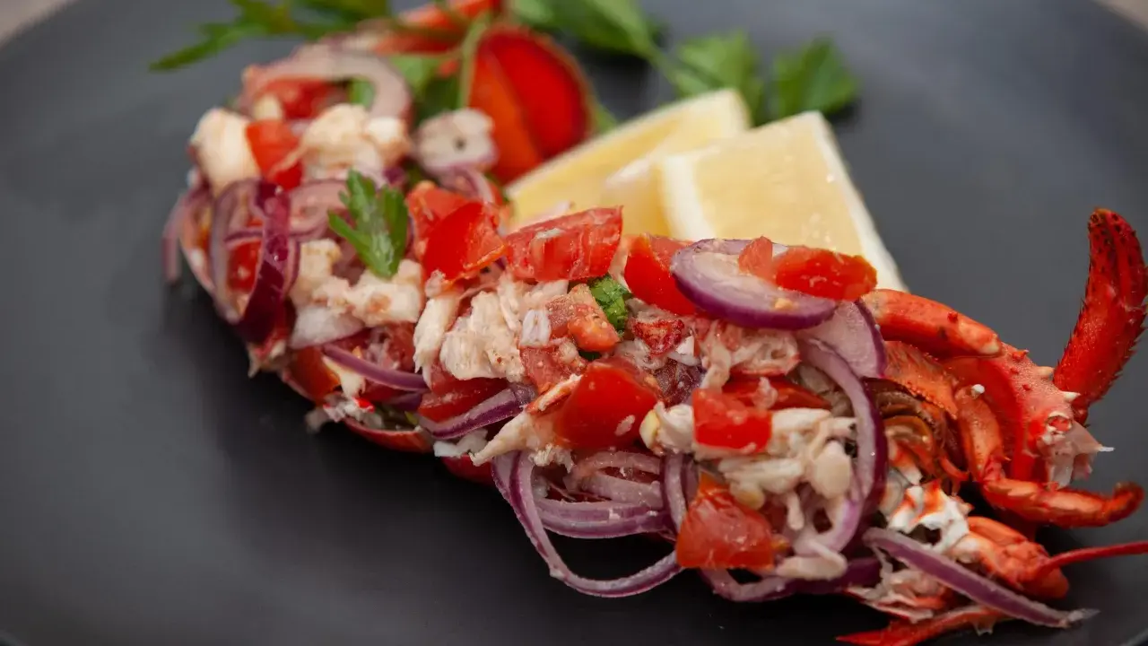 Astice alla catalana: un piatto fresco con astice, pomodoro, cipolla rossa e limone, guarnito con prezzemolo.