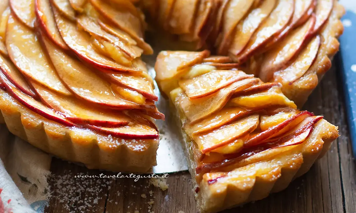 Una fetta di crostata di mele dorata, con mele caramellate disposte a rosa su una base friabile.
