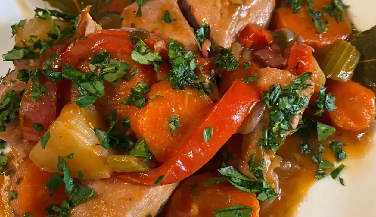 Un saporito spezzatino di pollo con carote, peperoni rossi e prezzemolo tritato, servito in un piatto bianco.