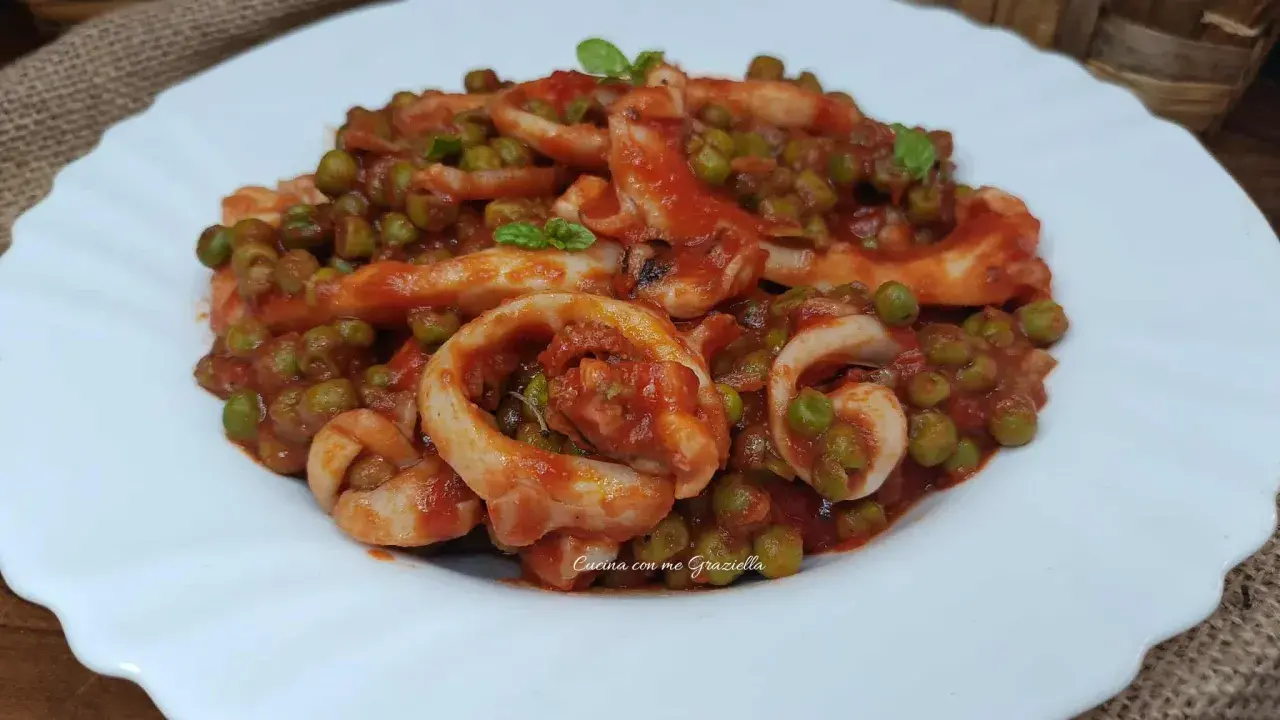 Un piatto invitante di seppie con piselli in umido, condito con una salsa rossa saporita e guarnito con basilico fresco.