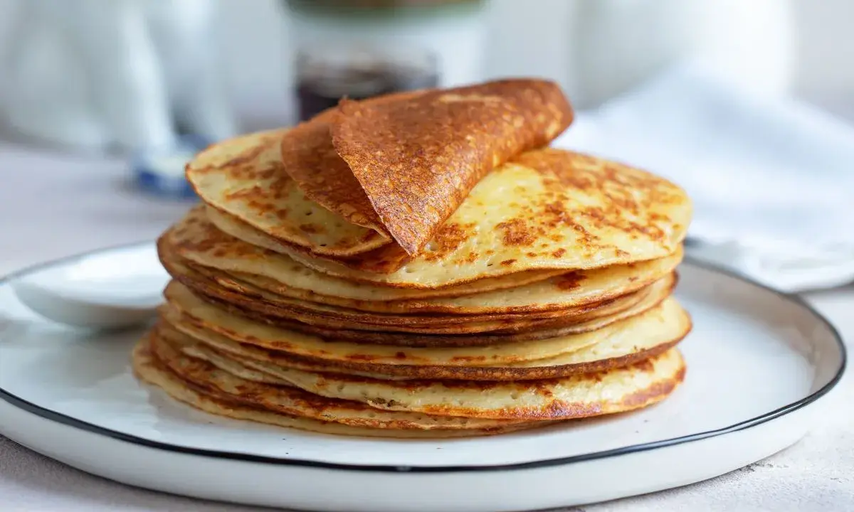 Una pila di dorate crepes senza glutine, una piegata in cima, su un piatto bianco.