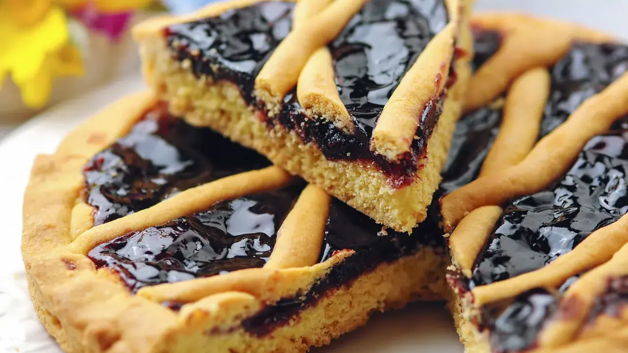 Una fetta di crostata di marmellata, con la sua base dorata e il ripieno scuro e lucido, pronta per essere gustata.