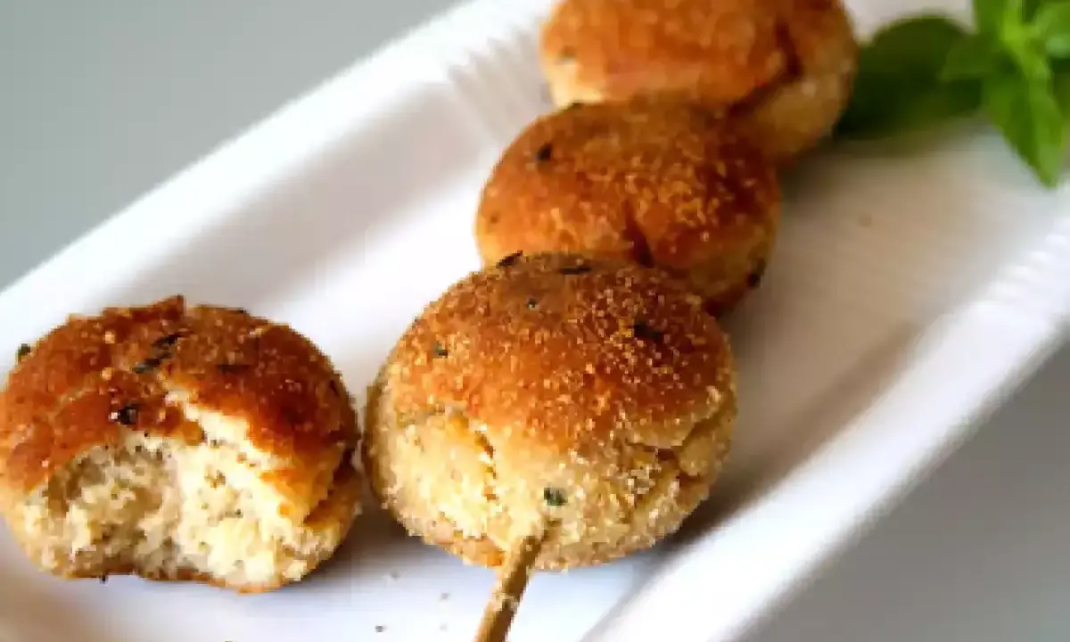 Polpette tonno e ricotta dorate su uno spiedino, una è stata morsa, con basilico fresco.