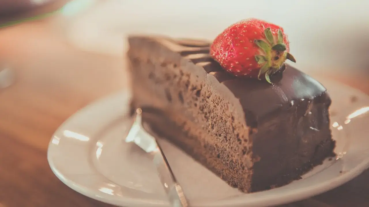 Una fetta di torta al cioccolato, ricoperta di glassa lucida e guarnita con una fragola fresca, pronta per essere gustata.