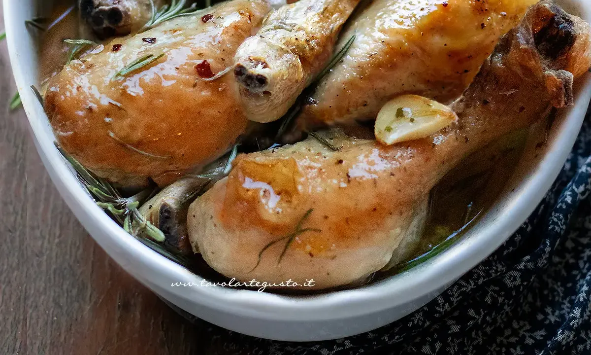 Succulente cosce di pollo al forno, dorate e profumate al rosmarino e aglio, servite in una ciotola bianca.