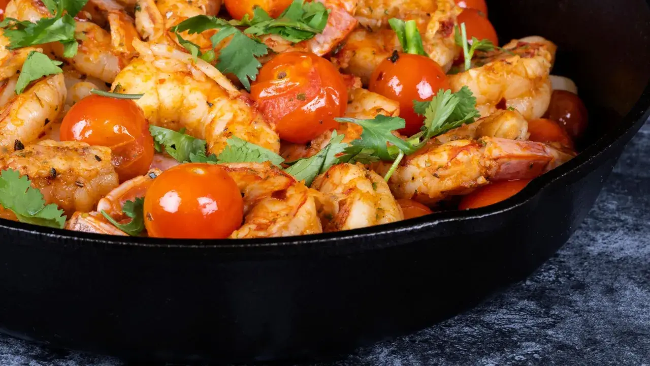 Gamberoni in padella succulenti, cotti con pomodorini e erbe aromatiche, un piatto invitante.