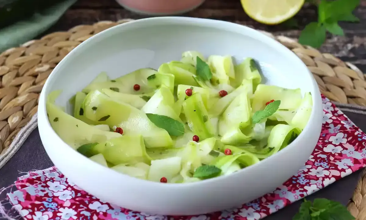 Delicate ribbons of zucchine marinate crude, tossed with fresh mint and pink peppercorns, served in a white bowl.