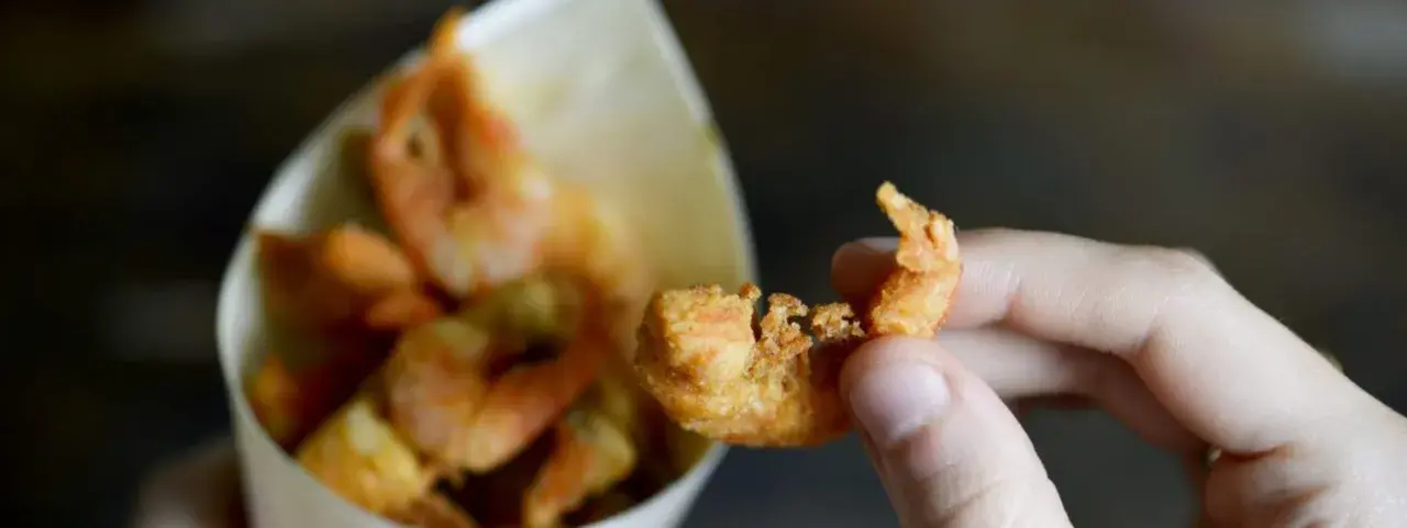 Una mano tiene un gambero croccante, parte di una deliziosa frittura di pesce servita in un cono di carta.