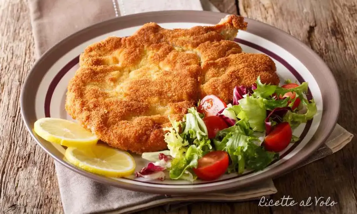 Cotoletta alla milanese dorata e croccante, servita con insalata fresca e spicchi di limone.