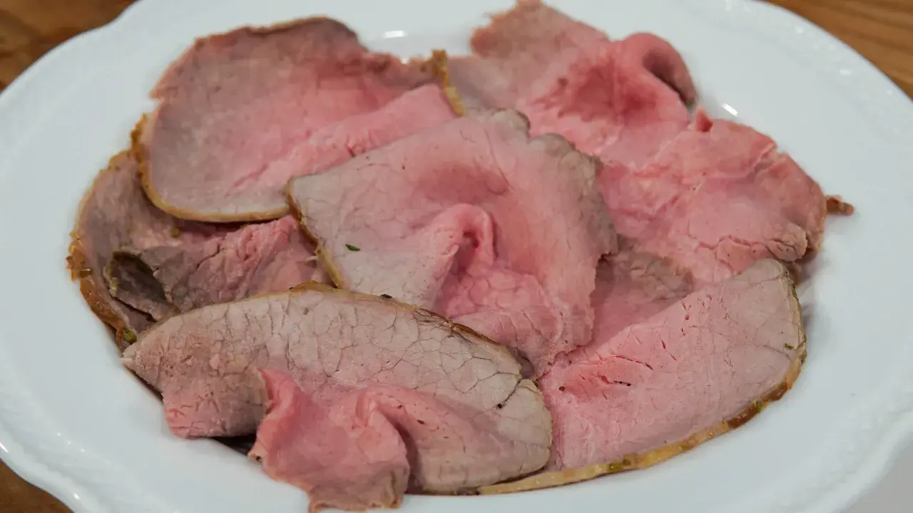 Fette sottili di arrosto di manzo rosa e succulento, servite su un piatto bianco.