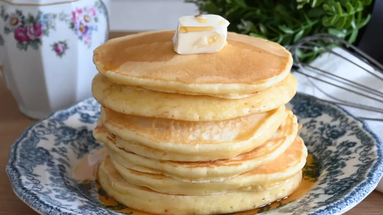 Pila di soffici pancake con farina di avena, guarniti con burro e sciroppo d'acero, su un piatto decorato.