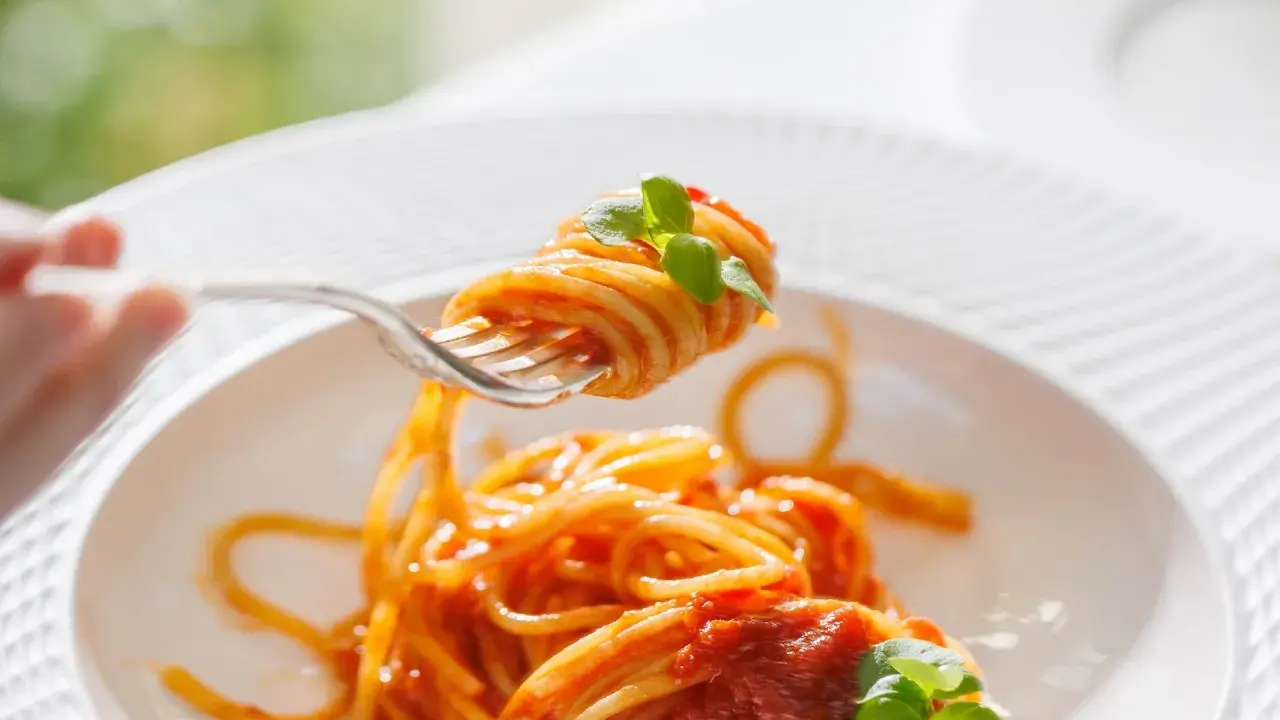 Un primo piatto invitante: spaghetti al dente conditi con un sugo rosso vivo di pomodorini freschi e basilico, pronti per essere gustati.