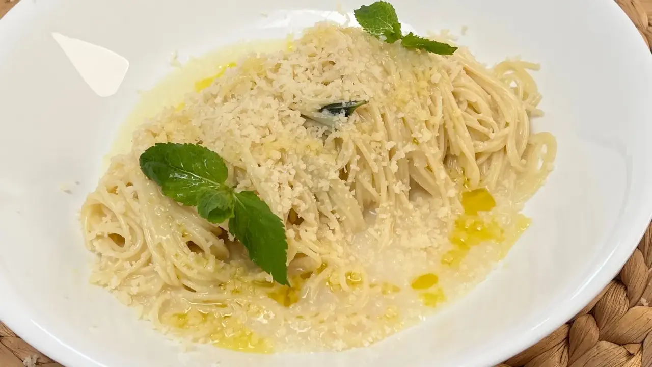 Spaghetti al limone cremosi, cosparsi di parmigiano e guarniti con foglie di menta fresca.