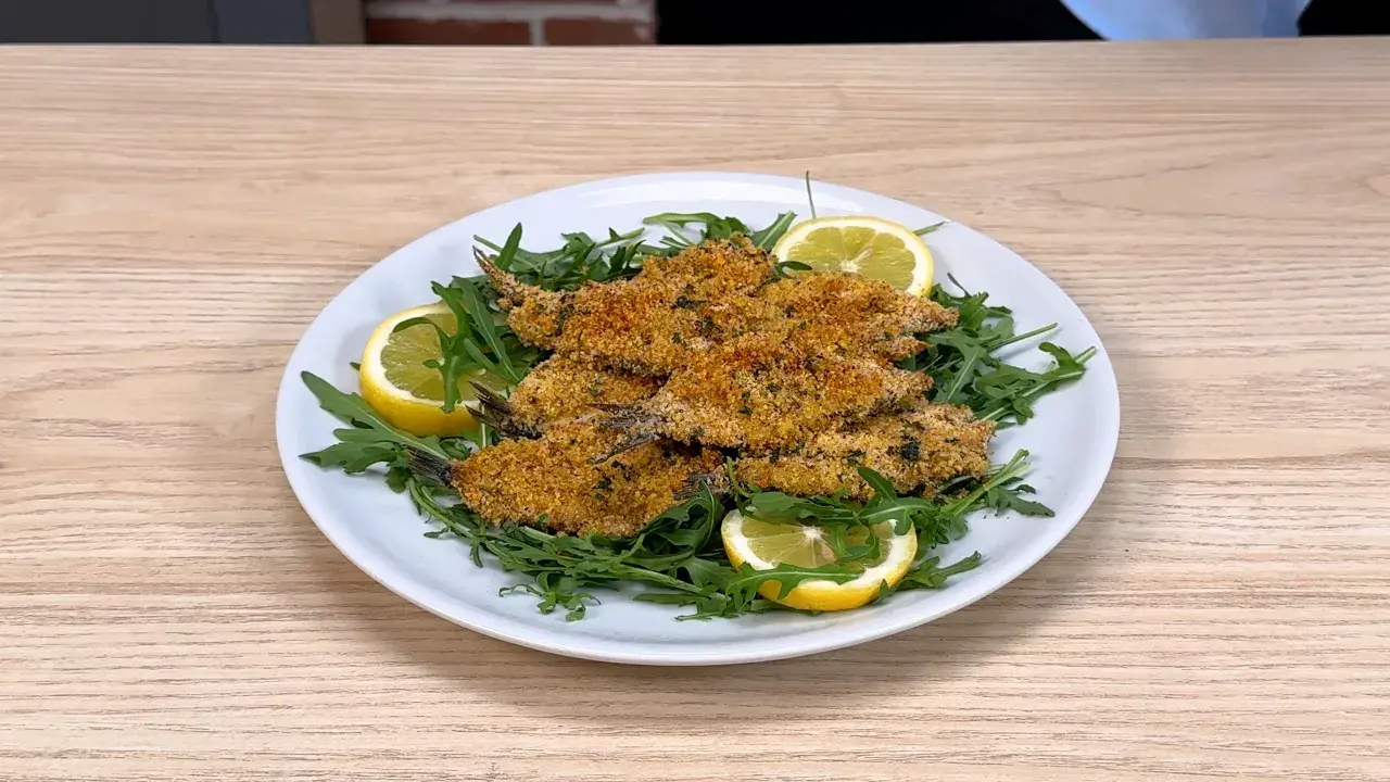 Piatto di alici al forno dorate e croccanti, servite su un letto di rucola fresca con spicchi di limone.
