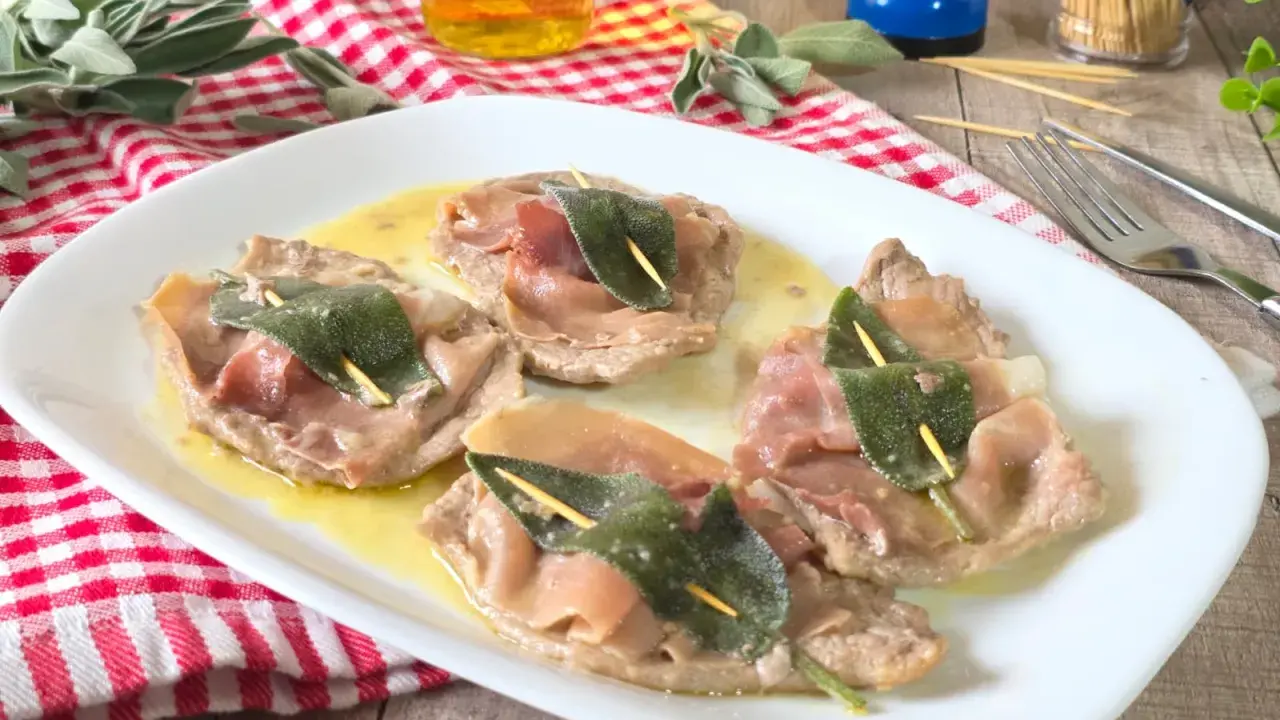 Saltimbocca alla romana su piatto bianco, con prosciutto crudo e salvia, su un tavolo di legno.
