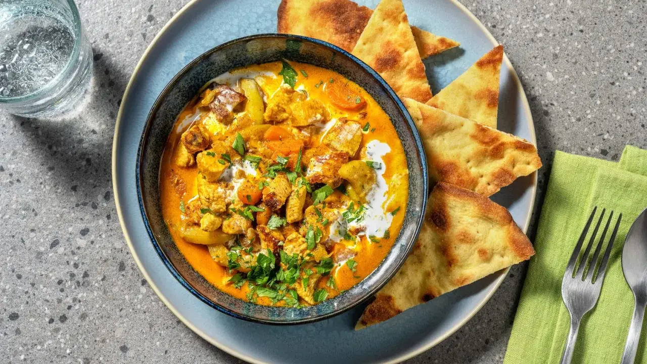 Un invitante pollo al curry cremoso, guarnito con coriandolo fresco e servito con pane naan croccante.