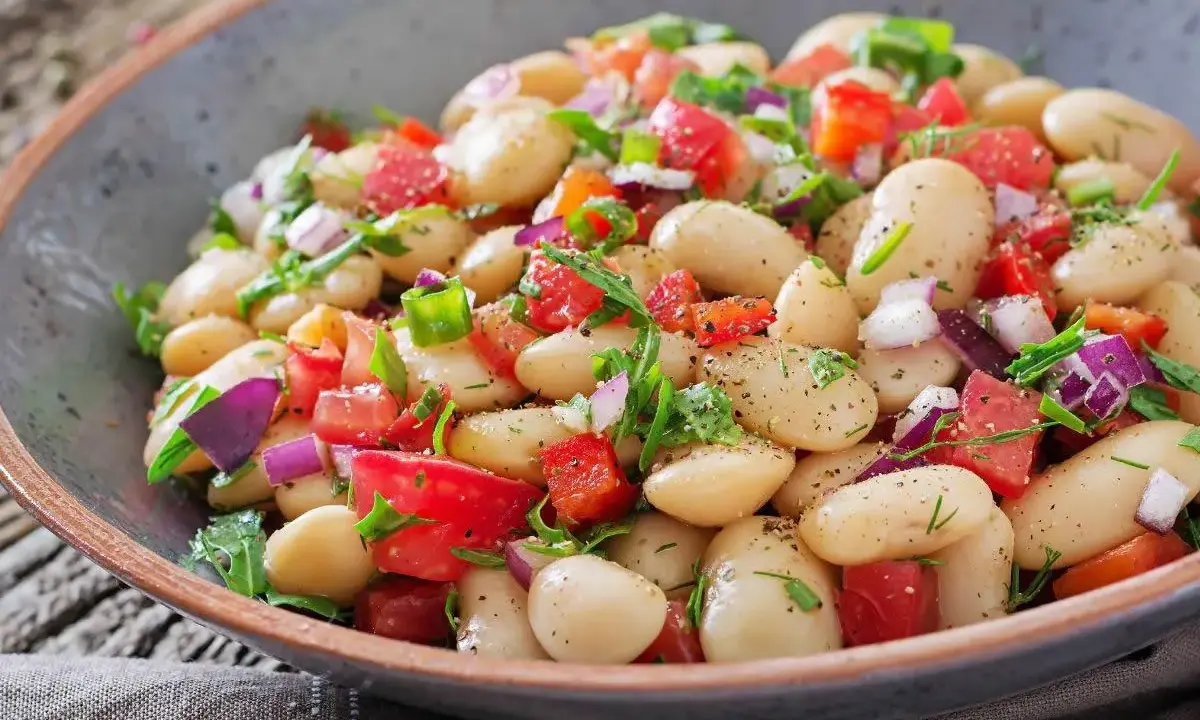 Insalata di fagioli bianchi, pomodori, cipolla rossa e erbe fresche in una ciotola rustica. Un piatto leggero e saporito.
