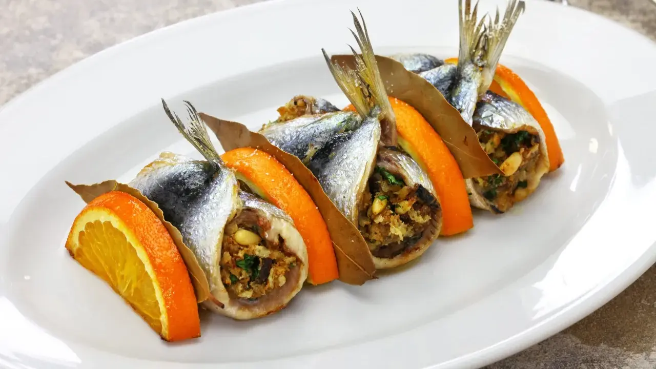 Sarde a beccafico, un piatto siciliano con sardine ripiene, arancia e alloro, servite su un piatto bianco.