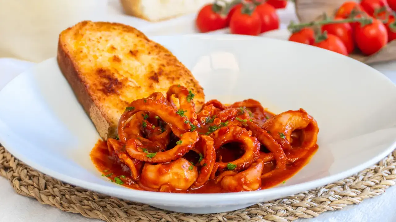 Moscardini in umido, teneri e saporiti, serviti con pane tostato e pomodorini freschi.