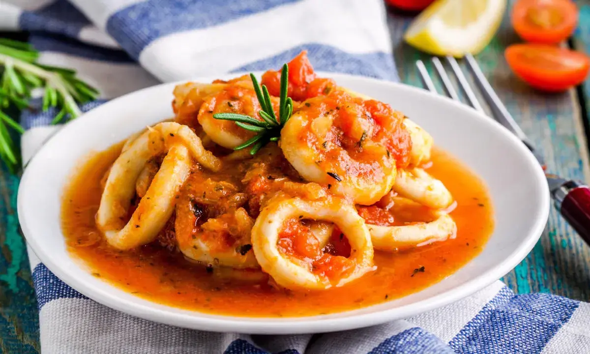 Calamari in umido succulenti, cotti in una salsa rossa saporita, guarniti con rosmarino fresco.