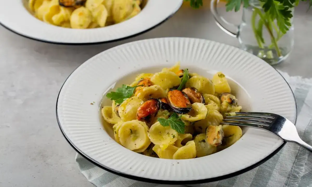 Orecchiette con patate e cozze, un piatto cremoso e saporito, guarnito con prezzemolo fresco.