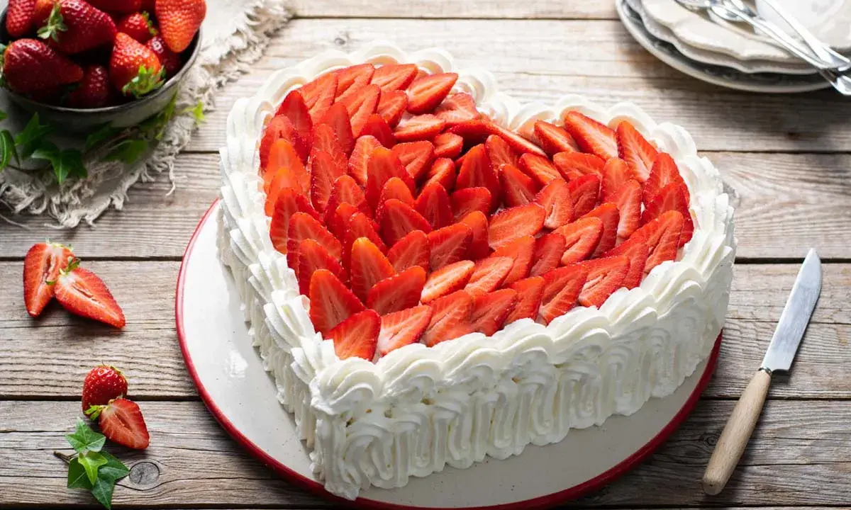 Cuore di torta panna e fragole, decorato con panna montata e fragole fresche a fette. Un invito alla dolcezza.