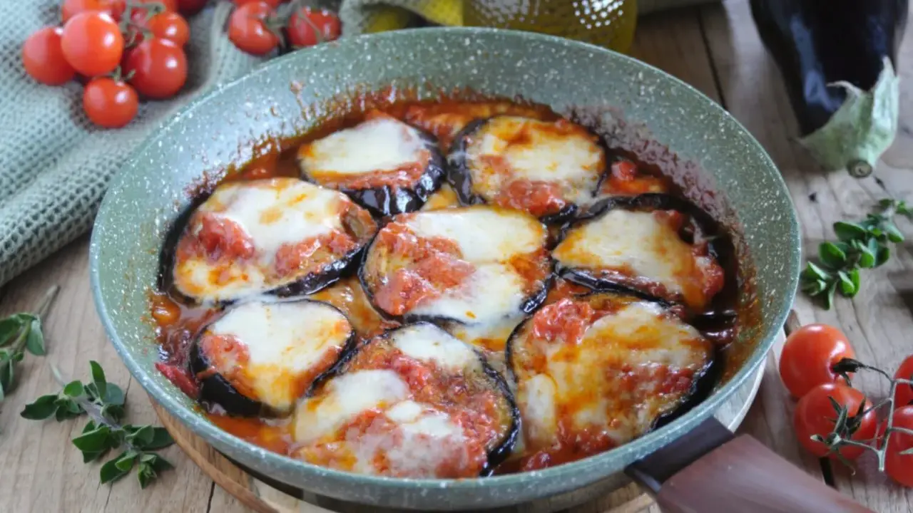 Melanzane alla pizzaiola in padella, con pomodoro e mozzarella filante, contornate da pomodorini freschi e basilico.