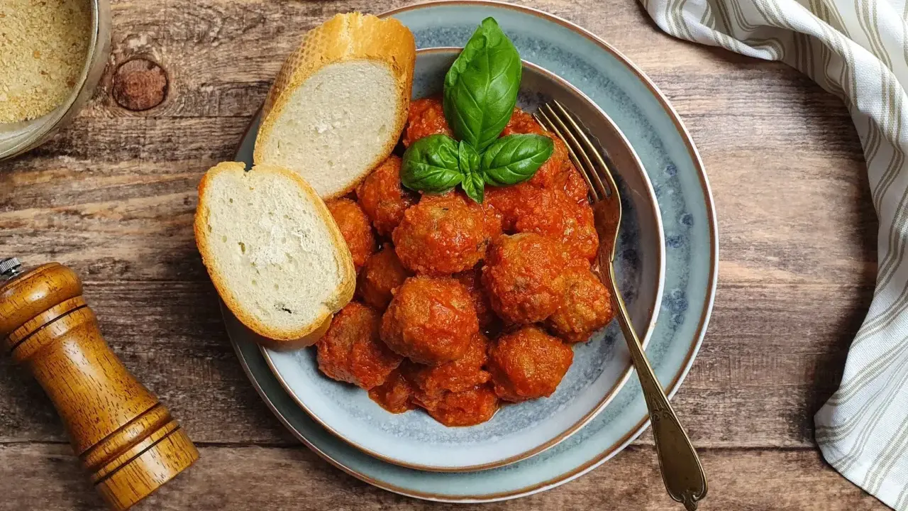 Succulente polpette al sugo, guarnite con basilico fresco, accompagnate da fette di pane croccante su un piatto blu.