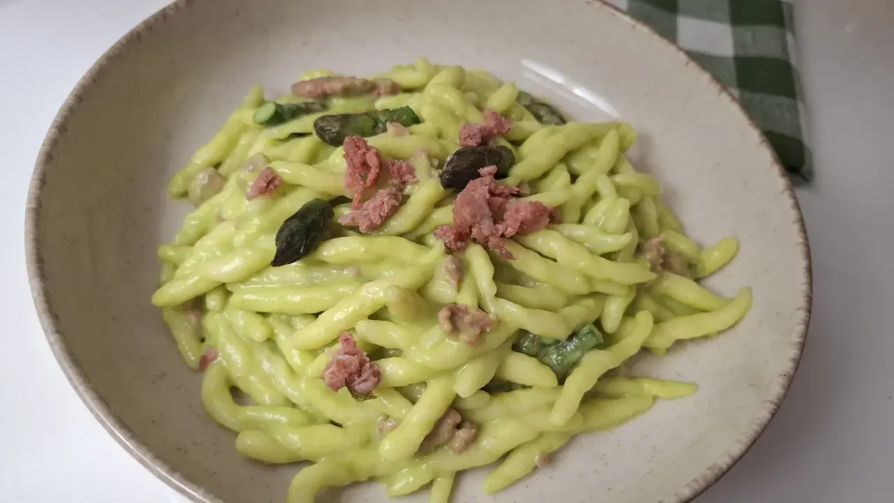Piatto di pasta fresca con crema di asparagi, pezzetti di salsiccia e punte di asparagi.