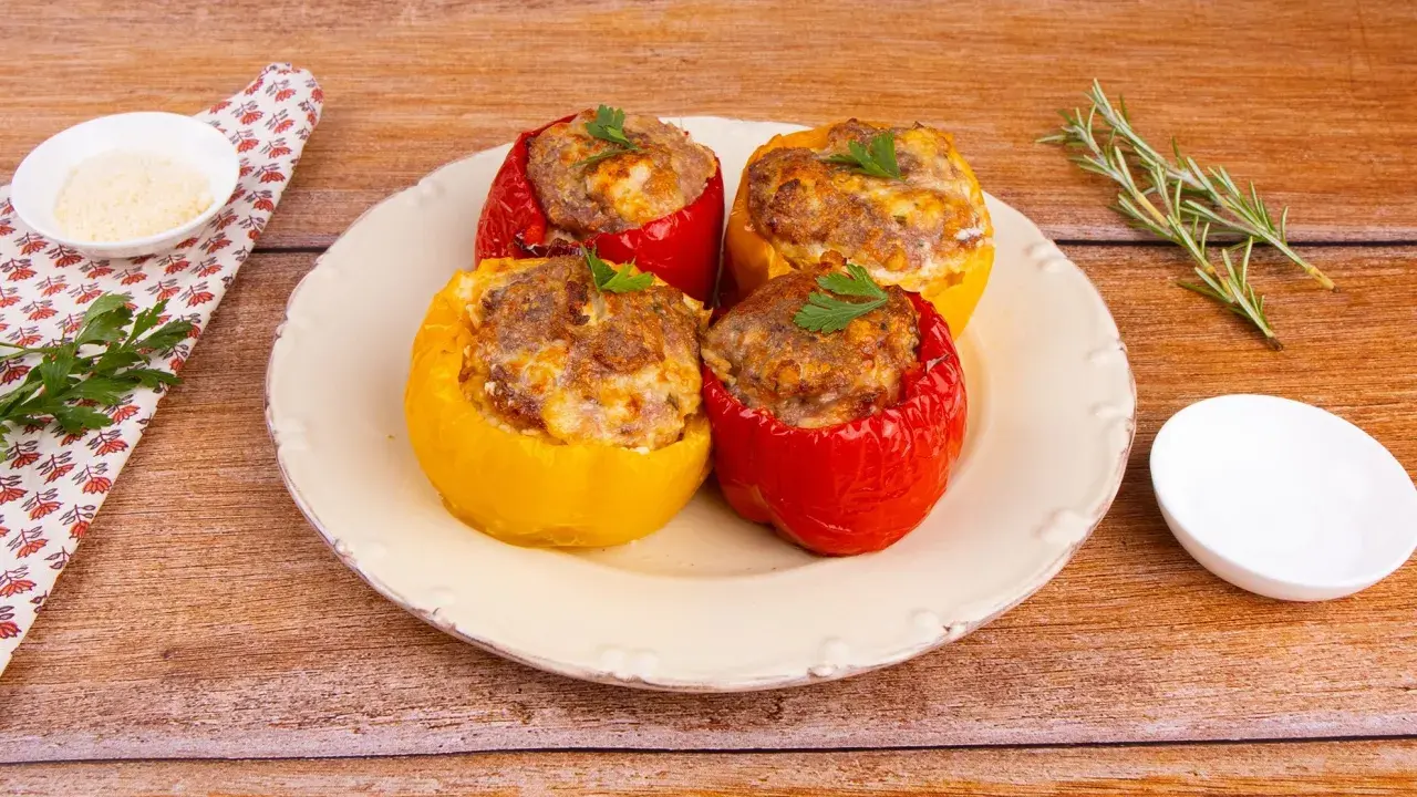 Quattro peperoni ripieni al forno, rossi e gialli, con un ripieno saporito e dorato, guarniti con prezzemolo fresco.
