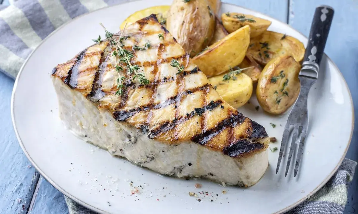 Un succulento trancio di pesce spada alla griglia, guarnito con timo fresco, servito con patate arrosto. Un'idea per le tue prossime ricette di pesce spada.