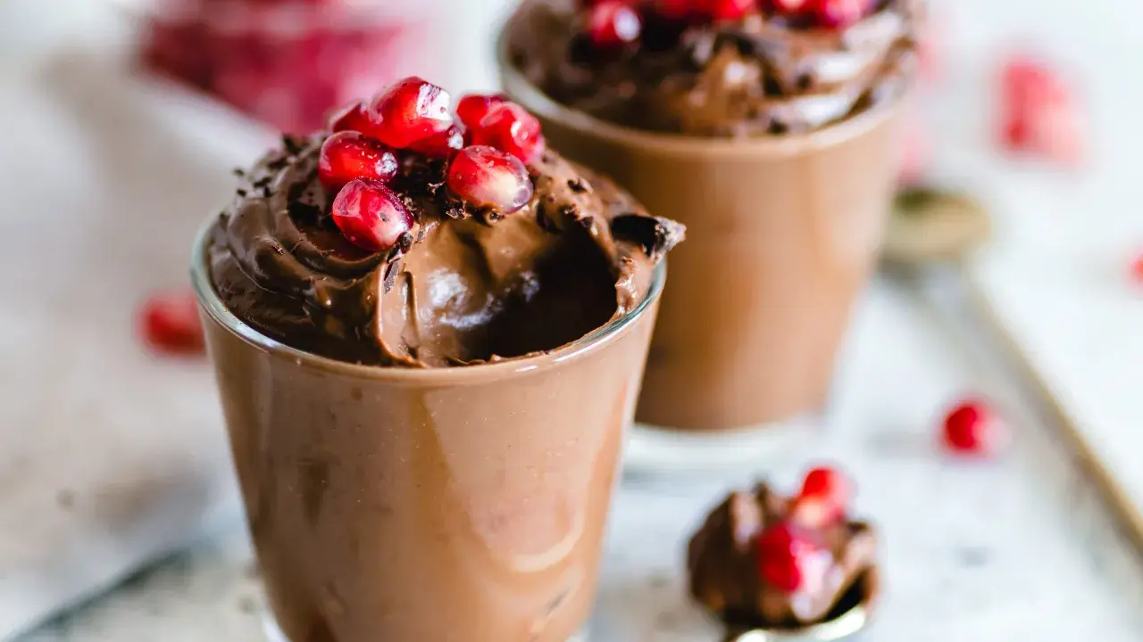 Due bicchierini di golosa mousse al cioccolato, guarniti con chicchi di melagrana e scaglie di cioccolato.