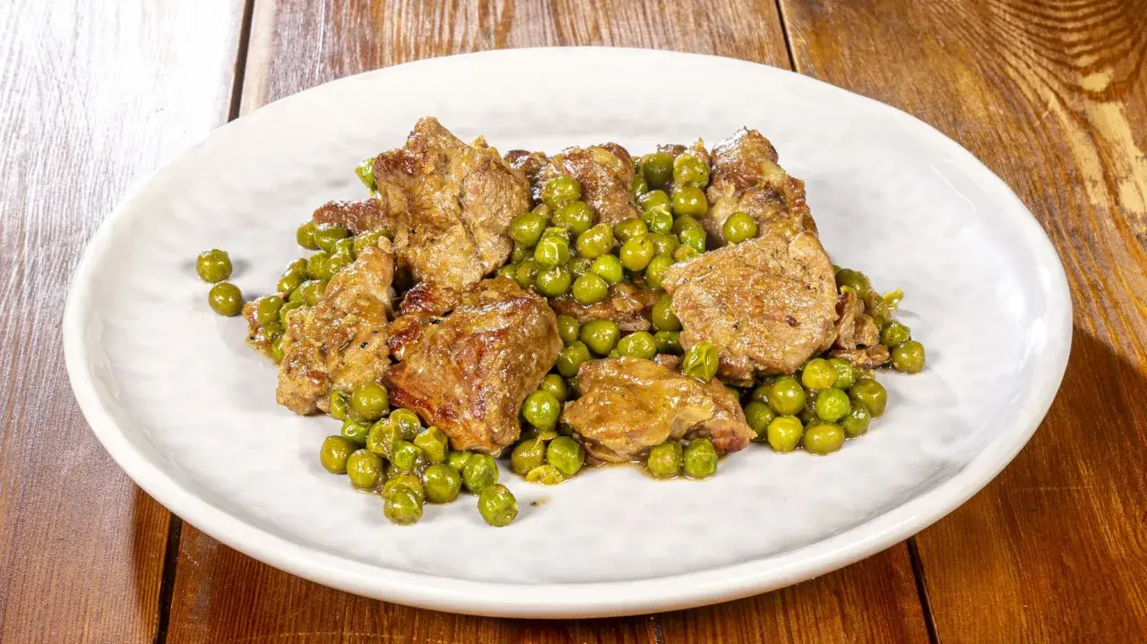 Un saporito agnello con piselli, un classico piatto italiano, servito su un piatto bianco.