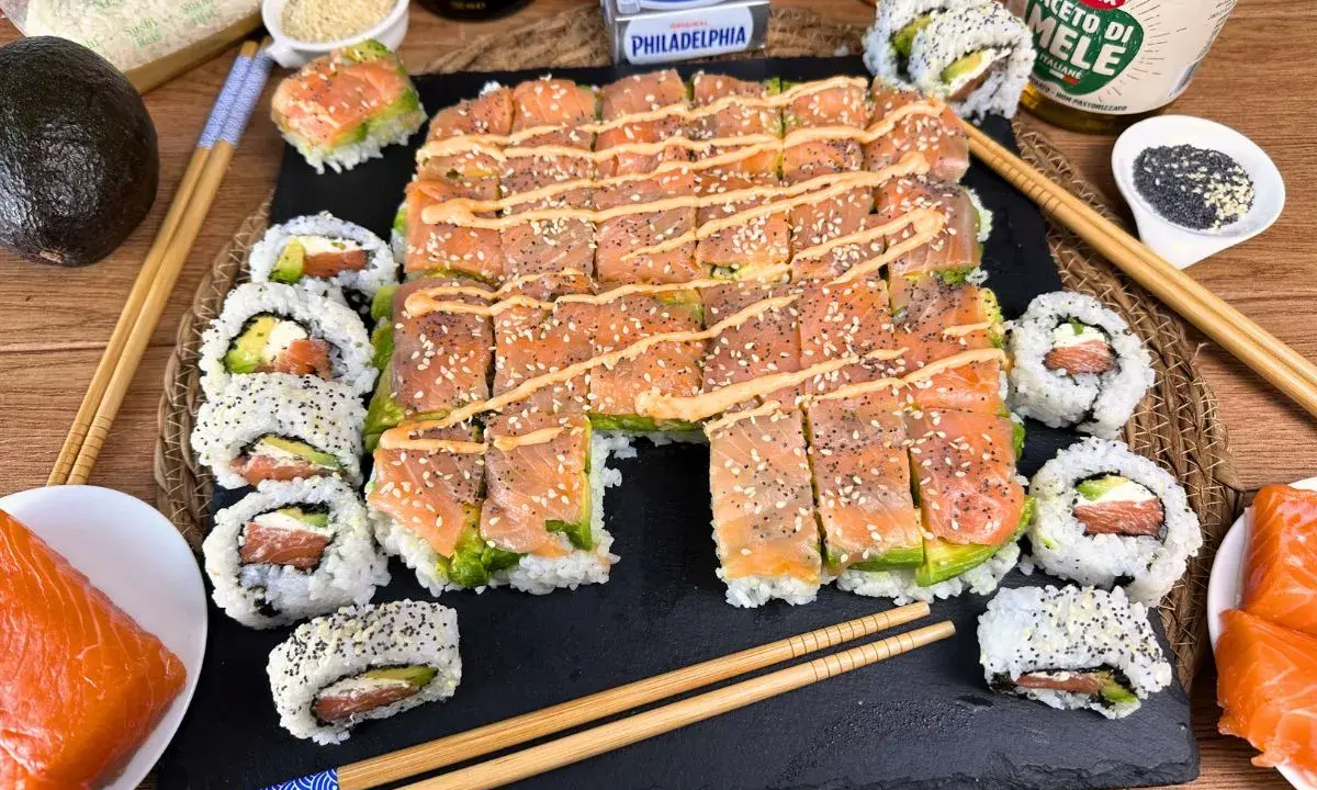 Un invitante sushi fatto in casa con salmone, avocado e formaggio Philadelphia, guarnito con semi di sesamo e una salsa cremosa.