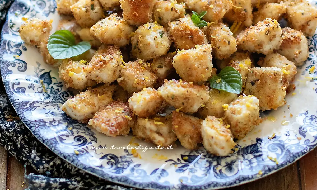 Bocconcini di pollo dorati e croccanti, guarniti con scorza di limone e foglie di menta fresca su un piatto decorato.
