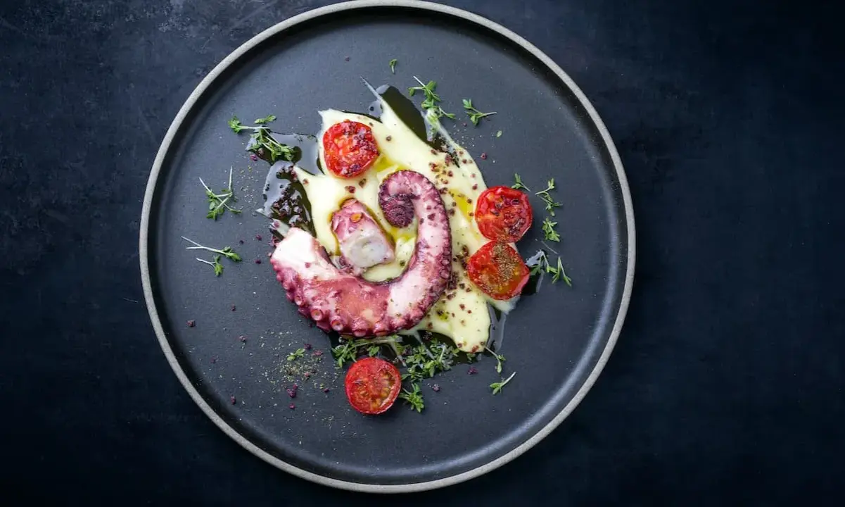Un tentacolo di polpo alla griglia, servito su purè di patate con pomodorini confit e timo fresco.