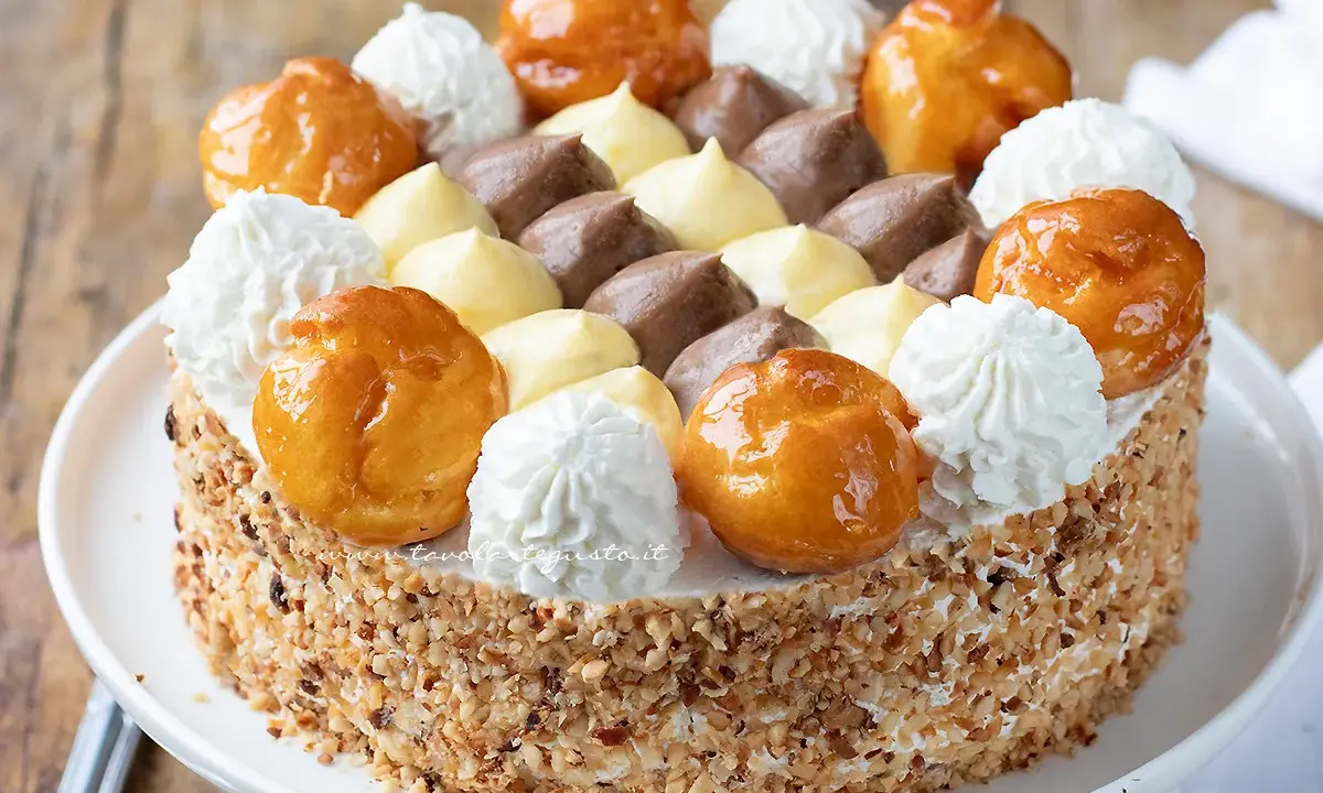Torta Saint Honoré decorata con bignè caramellati, ciuffi di panna montata e crema pasticcera al cioccolato e vaniglia.