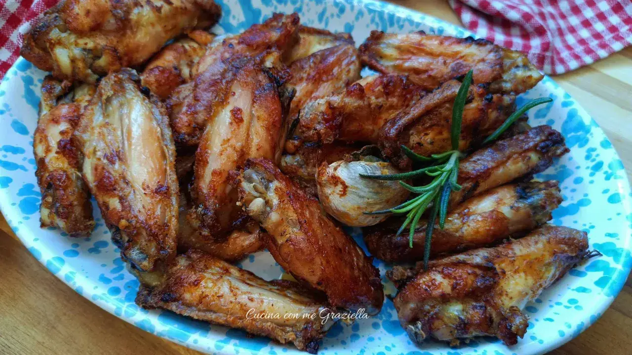 Alette di pollo dorate e croccanti, servite su un piatto decorato con un rametto di rosmarino.