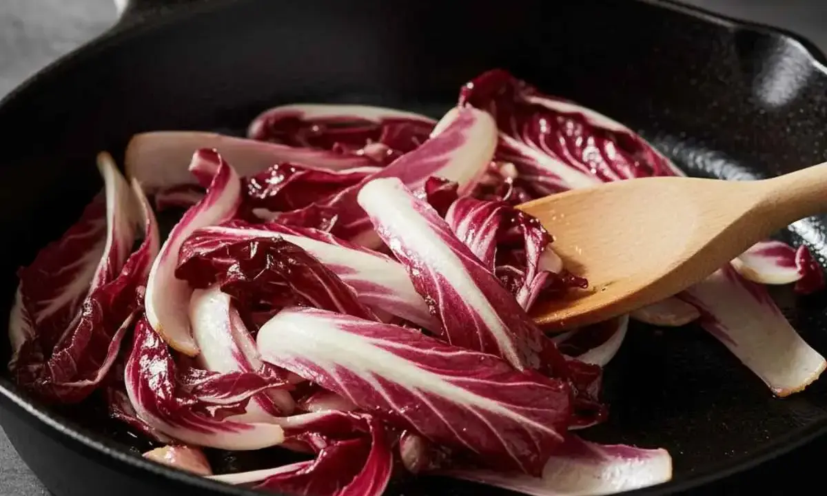 Fette di radicchio rosso vengono saltate in padella con un cucchiaio di legno.